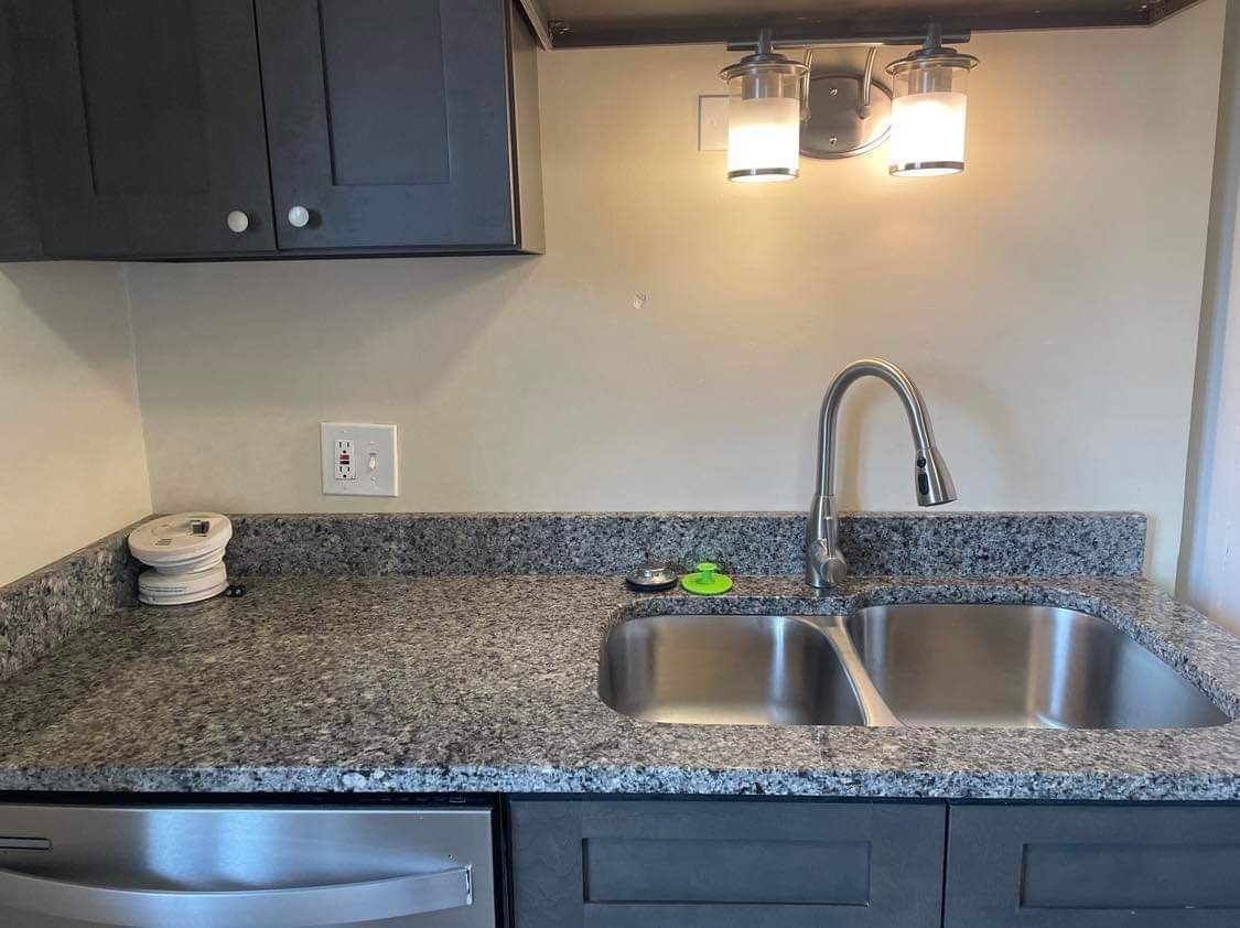 Modern kitchen sink with gray granite countertop, faucet, and under-cabinet lighting.