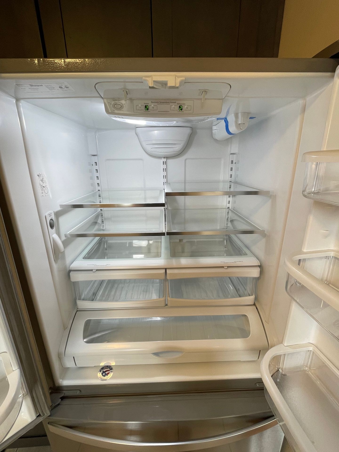 Open empty refrigerator with glass shelves and a control panel at the top.