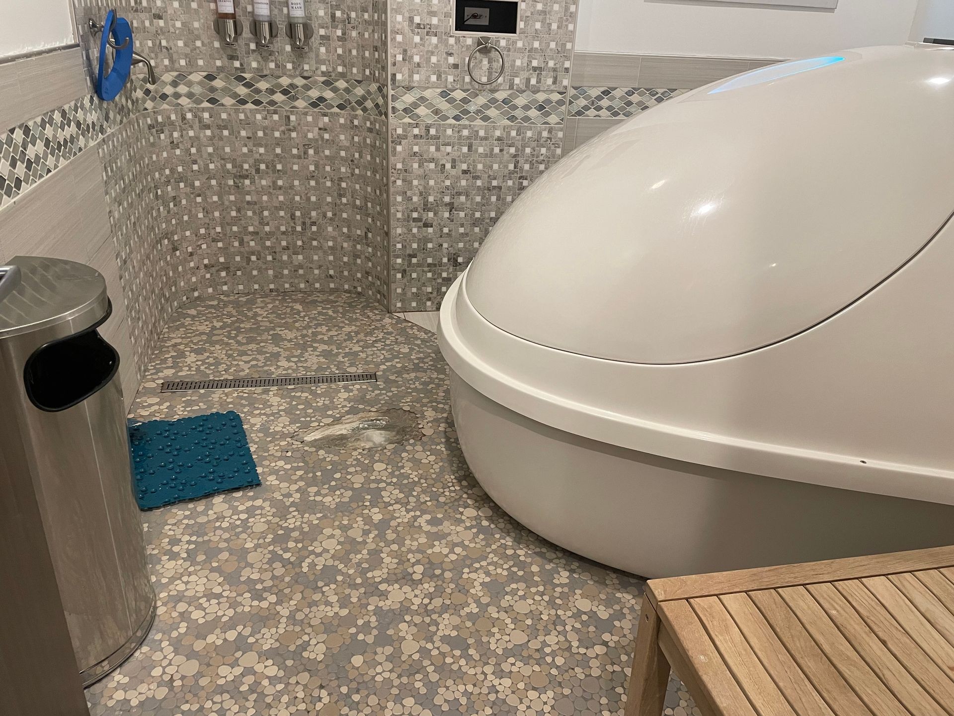 Relaxation room with sensory deprivation tank, patterned tile floor, and wall-mounted dispensers.